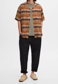 Kortærmet strikket skjorte med flerfarvede geometriske mønstre, beige bomulds t-shirt under, sorte bukser og lysebrune slip-on sko.