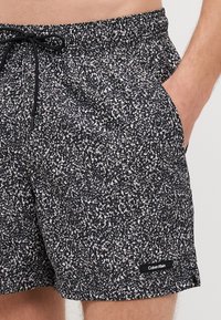 Čierne plávacie šortky s bielym bodkovaným vzorom, elastický pás, detail so šnúrkou a bočné vrecká. Štítok s logom Calvin Klein na leme.