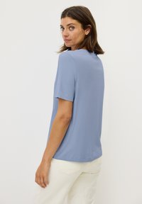 Camiseta de manga corta de color azul claro, hecha de tela suave, con un escote redondo y un corte relajado. Combinada con pantalones blancos.