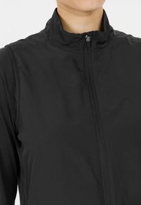 Svart zip-up jacka med hög krage, tillverkad av ett mjukt, lätt tyg. Har en subtil glans och en minimalistisk design.