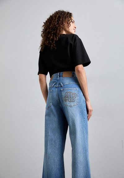 Széles szárú kék farmernadrág magas derékkal és jellegzetes hímzett logóval a hátsó zseben. Fekete, cropped pólóval párosítva.