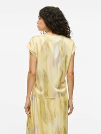 Top in satin con maniche corte, caratterizzato da un motivo astratto giallo e verde pastello, texture liscia e vestibilità rilassata, mostrato da dietro.