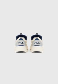 Ett par beige och marinblå FILA-sneakers visade från baksidan mot en vit bakgrund.