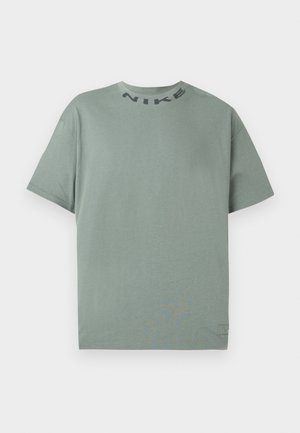 Világoszöld, rövid ujjú Nike póló kerek nyakkal, fekete "NIKE" felirattal a gallér közelében, sima fehér háttérrel.