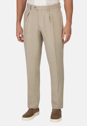 Pantalones de color beige claro con un acabado texturizado, con cierre de botón y dos pliegues en la parte delantera. Combinados con zapatillas marrones para un look casual.