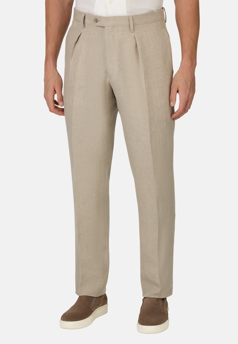 Pantalons beige clair avec une finition texturée, dotés d'une fermeture à bouton et de deux plis à l'avant. Associés à des baskets brunes pour un look décontracté.