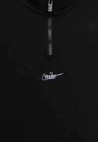 Sudadera negra con cremallera hecha de una tela texturizada, que cuenta con un cuello alto y un logo de Nike bordado en blanco en el lado izquierdo.