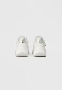Bijele tenisice s metalik srebrnim akcentima, glatkom teksturom i zaobljenim oblikom. Imaju podstavljeni ovratnik i suptilni detalj loga na peti.