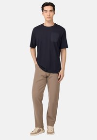 Námořnické tričko s krátkým rukávem a kapsou na prsou, spárované se světle hnědými kalhotami a béžovými teniskami, postavené proti čistému bílému pozadí.