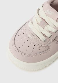 Sneakers Nike con una toma superiore in pelle lavanda liscia, punta perforata, lacci crema e suola in gomma bianca testurizzata.