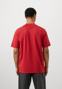 Κόκκινο κοντομάνικο πουκάμισο με λεία υφή, που διαθέτει μια διακριτική ραφή στην πλάτη και στρογγυλή λαιμόκοψη. Συνδυασμένο με σκούρα τζιν.