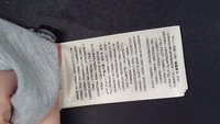 Étiquette de vêtement avec informations multilingues sur le tissu et la fabrication tenue entre les doigts sur fond sombre.