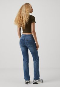 Blå denimjeans med rett snitt, middels vask og subtil falming; kombinert med en tettsittende olivengrønn topp og sølvfargede joggesko.