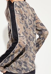 Langarmtop met een luipaardprint in beige en zwart, met contrasterende zwarte mouwen en witte biesdetails langs de naden.