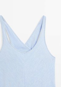 Haut bleu clair sans manches avec bretelles croisées dans le dos, en tissu doux, présenté sur fond blanc.