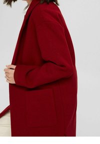 Czerwony wełniany płaszcz o dopasowanym kroju, z klapowanym kołnierzem i pojedynczą kieszenią. Materiał ma gładką fakturę, ukazaną na widoku z boku.
