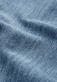 Ljusblå denimtyg med twillväv, som visar en jämn struktur och subtila diagonala mönster, med viss blekning och slubbar.