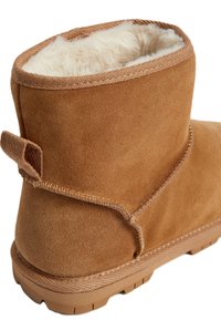 Bottine en daim marron avec un intérieur doux en fourrure, dotée d'une bride de traction en boucle et d'une semelle en caoutchouc texturée pour une meilleure adhérence.