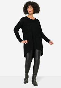 Black long-sleeve tunic with a rounded hem, paired with shiny black leggings and studded black ankle boots, showcasing a relaxed fit.