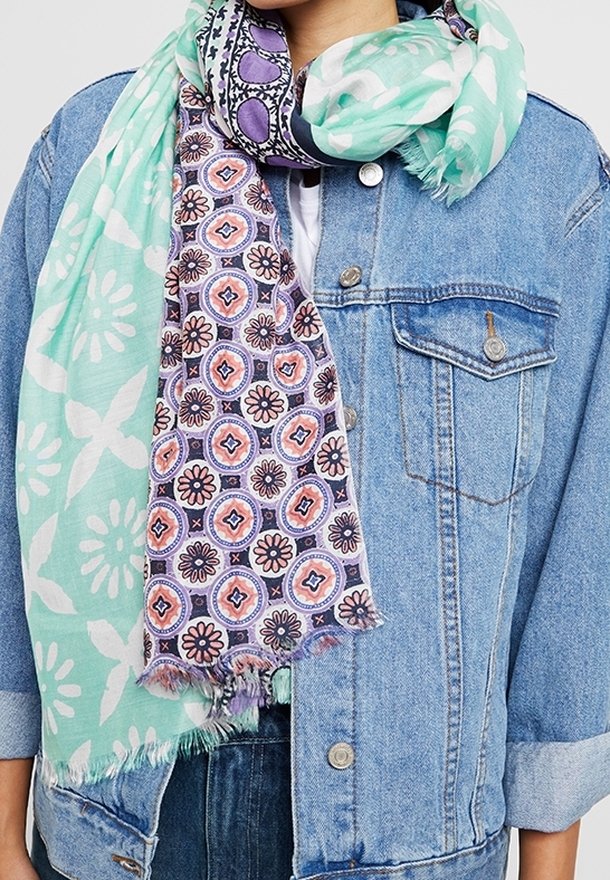 Veste en jean bleu clair avec manches retroussées, associée à une écharpe à double motif enroulée présentant des motifs floraux vert menthe et violet.