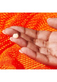 White cream globule resting on an outstretched palm, against a textured bright orange background. Smooth, viscous appearance.