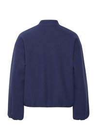 Tumši zils pulovers ar augstu apkakli, nokritušiem pleciem un savilktiem piedurkņu galiem. Mīksta auduma ar gludu tekstūru, īsāks apakšmala.