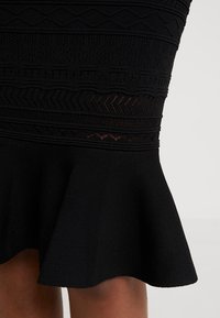 Jupe en tricot noir avec des motifs texturés, un ourlet évasé et un mélange de sections unies avec des découpes géométriques.