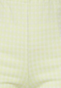 Tecido amarelo claro quadriculado com pequenos quadrados brancos, apresentando uma textura suave e costuras visíveis.