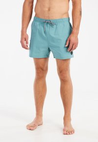 Tyrkysové plavky s elastickým pásom a čiernym šnurovaním, na bočných stranách s vreckami a s logom na ľavom stehne.