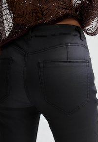 Black skinny jeans with a smooth texture, featuring back pockets, decorative stitching, and a sleek design.