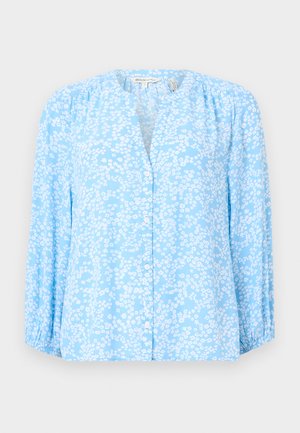 Blouse bleu clair avec motif floral blanc, manches longues, col rond et devant boutonné. Tissu doux avec une légère texture et des détails froncés.