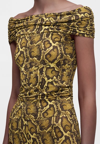Femme portant une robe épaules dénudées avec un motif serpent jaune et noir et des détails froncés sur les manches et la taille.