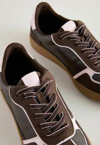 Sneaker marroni con accenti rosa e dettagli bianchi, con lacci e una suola testurizzata, esposti su uno sfondo chiaro.