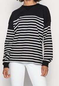 Schwarz-weißer gestreifter Langarmtop mit V-Ausschnitt und fallenden Schultern, aus weichem Stoff gefertigt. Die Bündchen sind einfarbig schwarz.