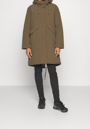 Braune Parka mit Kapuze, zwei Fronttaschen, Tunnelzug in der Taille und legerer Passform. Kombiniert mit schwarzen Slim-Fit-Hosen und schwarzen Schuhen.