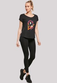 Svart T-skjorte med korte ermer som har et fargerikt Wonder Woman-trykk, parret med svarte leggings og svarte joggesko. Mykt stoff, avslappet passform.