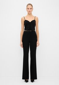 Top negro corto con tirantes finos, combinado con pantalones de pierna ancha de talle alto en negro. Textura suave; diseño ajustado; estilo minimalista.