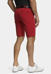 Shorts rouges en tissu lisse avec une coupe slim, dotés de deux poches arrière et d'un accent ceinture noire. Portés avec des chaussures de sport blanches.