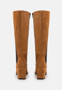Braune Wildleder-Stiefel in Knielänge mit einem stabilen Absatz und seitlichem Reißverschluss, versehen mit einem kontrastierenden elastischen Einsatz an der Außenseite für mehr Flexibilität.