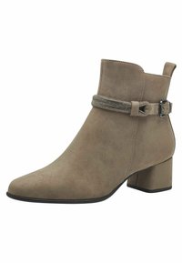Bottine en suède beige avec un talon bloc, bout pointu et une sangle décorative avec des embellissements métalliques autour de la cheville.