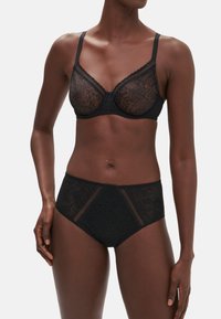 Svart spetsbehå med underwire och justerbara axelband, i kombination med högmidjade trosor som har ett texturerat mönster och genomskinliga detaljer.
