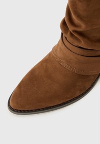 Brown suede ankle boot with a pointed toe, gathered design at the top, and visible stitching on the side and sole.