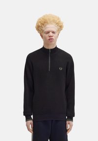 Maglione zip-up nero con tessuto texturizzato, colletto alto e polsini a coste, con un piccolo logo verde sul petto.