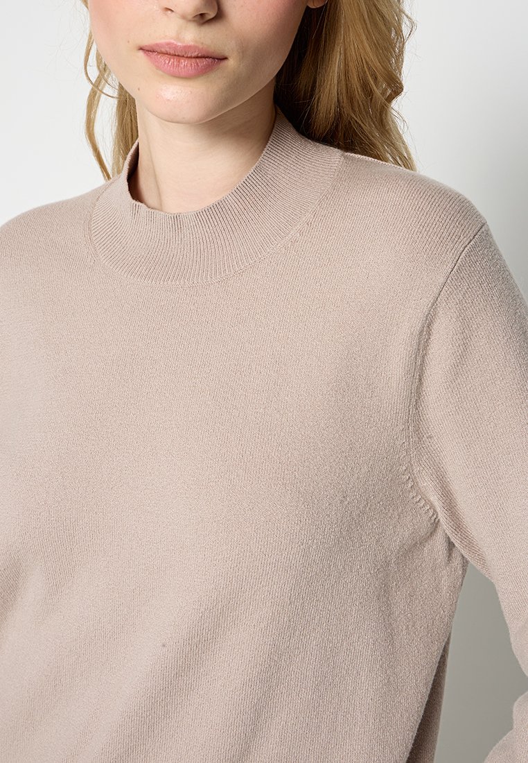 Hellbeige Pullover mit einem gerippten hohen Kragen, aus weichem Strickmaterial gefertigt. Nahtlose Schultern und eine lockere Passform.