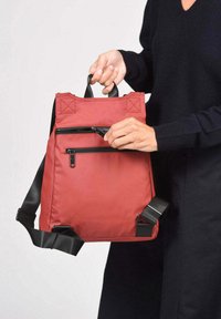 Rode nylon rugzak met verstelbare zwarte banden, voorvak met rits en bovenhandvatten. Gladde textuur en minimalistisch ontwerp.