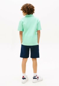 Polo shirt verde chiaro a maniche corte, abbinato a pantaloni navy. L'outfit presenta una vestibilità rilassata ed è completato da sneakers bianche con accenti.