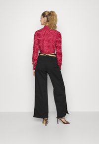 Blusa curta vermelha com estampado animal texturizado, combinada com calças largas pretas com fendas laterais e sandálias de salto pretas.