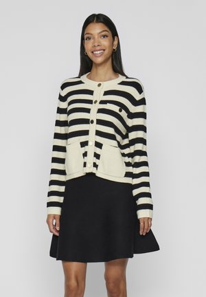 Mustri must ja koorega kardigan, millel on ümmargune kaelus, ees nupud ja kaks taskut, valmistatud ribakujulisest kangast. Kandub musta seeliku üle.