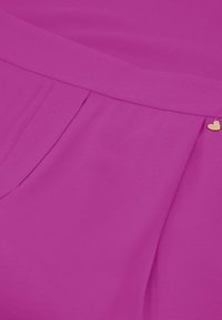 Fuchsia geplisseerde jurk met een soepele textuur, voorzien van een gouden hartaccent nabij de taille.
