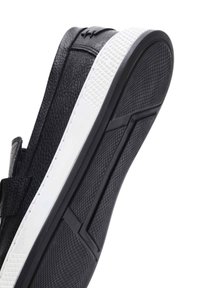 Zwarte leren schoen met een gestructureerde afwerking, voorzien van een witte rubberen zool en een patroonprofiel voor grip. Geaccentueerd met een minimalistisch ontwerp.